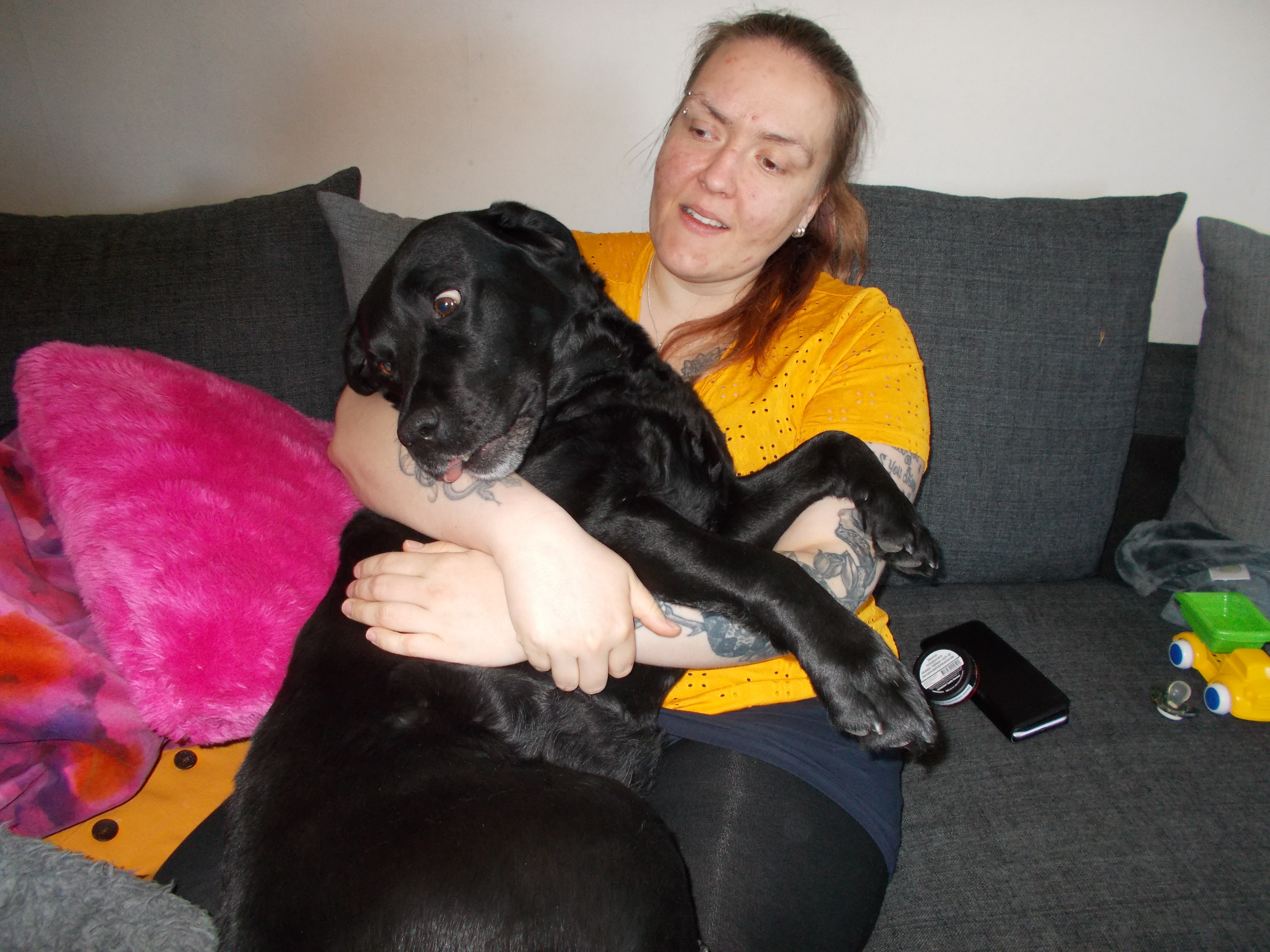 Ida sitter i soffan med labradoren Stella i sin famn. En barnleksak ligger bredvid i soffan.