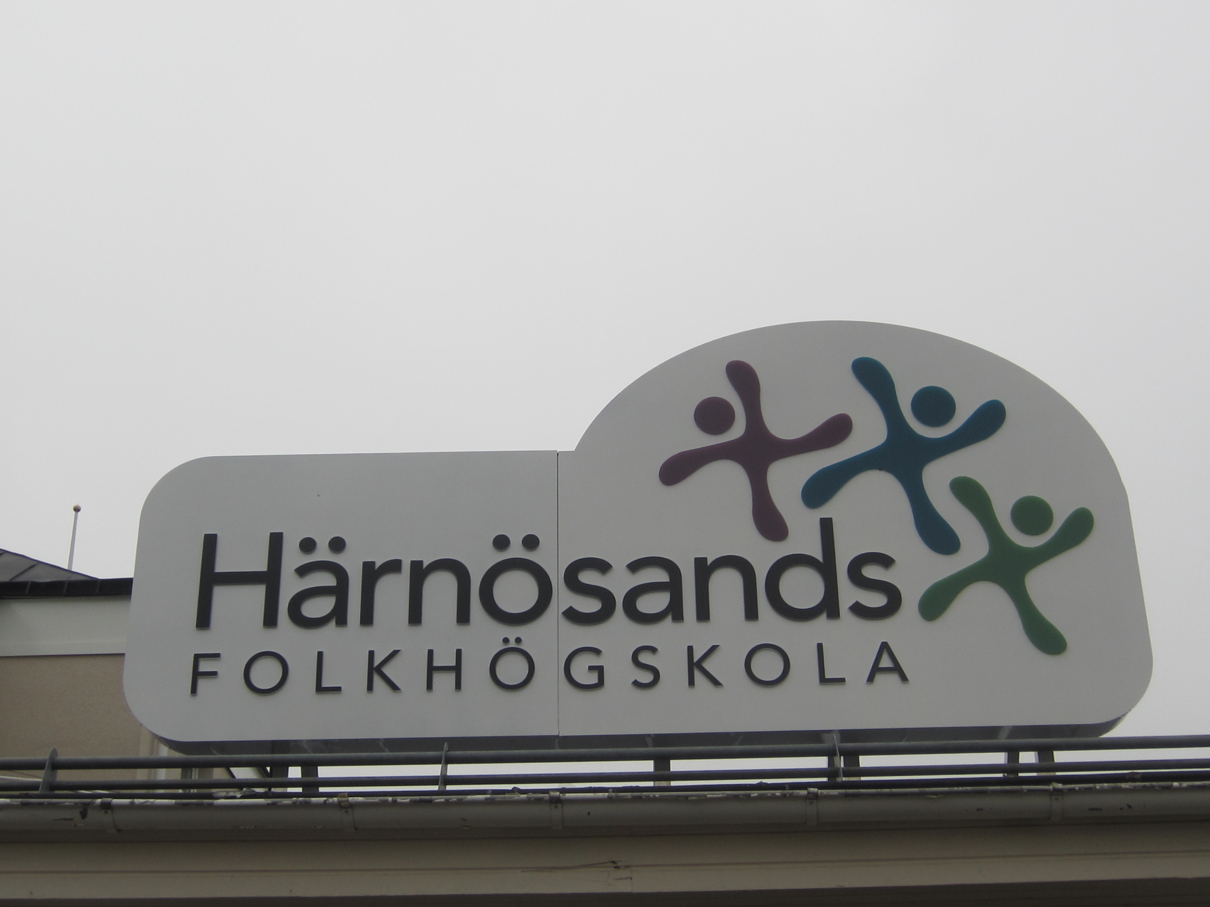 Tak skylten med texten Härnösands folkhögskola tonar upp sig mot en gråmulen himmel