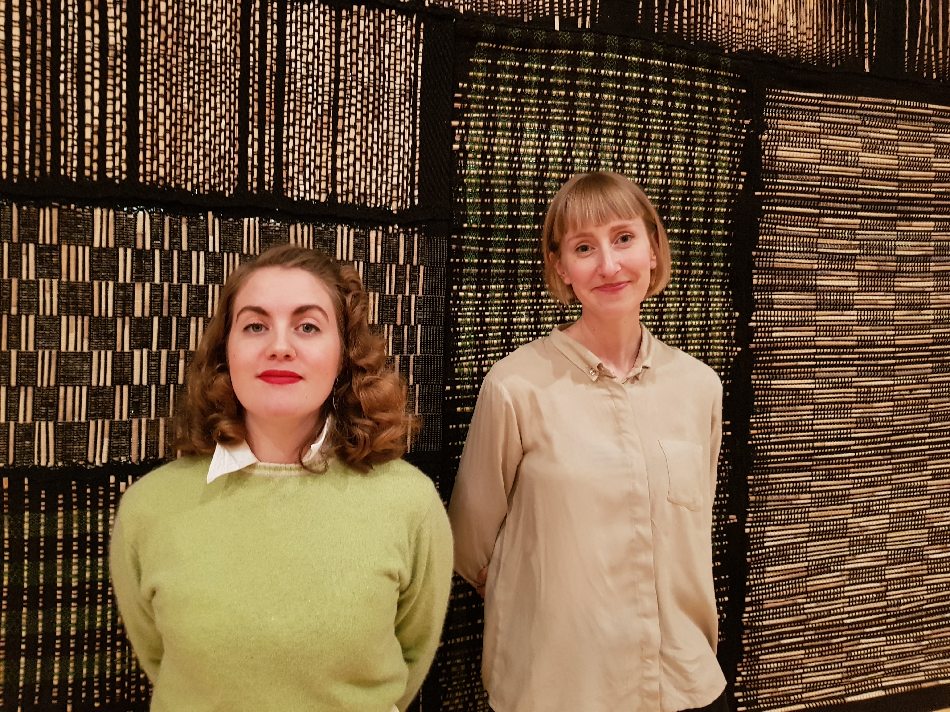 Mirjam Parkman och Mirjam Hemström poserar framför en vävd hängande matta i utställningslokalen vid Västernorrlands museum