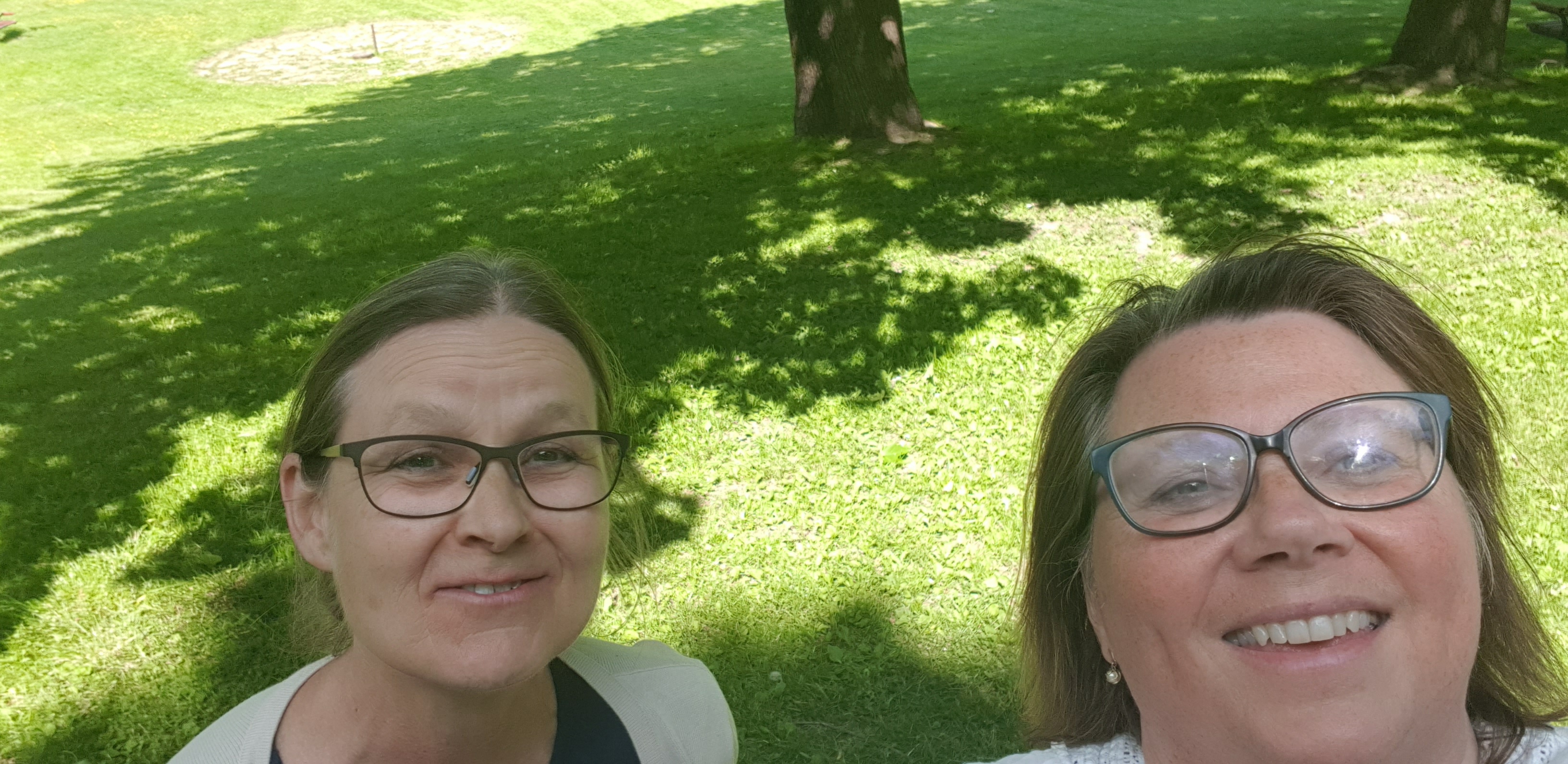 Monica och Anette bär båda glasögon. De står i en grönskande park och ler mot kameran