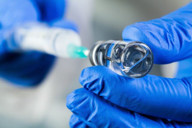 En vaccinationsspruta fylls på med vaccin. Sköterskan bär blå skyddshandskar