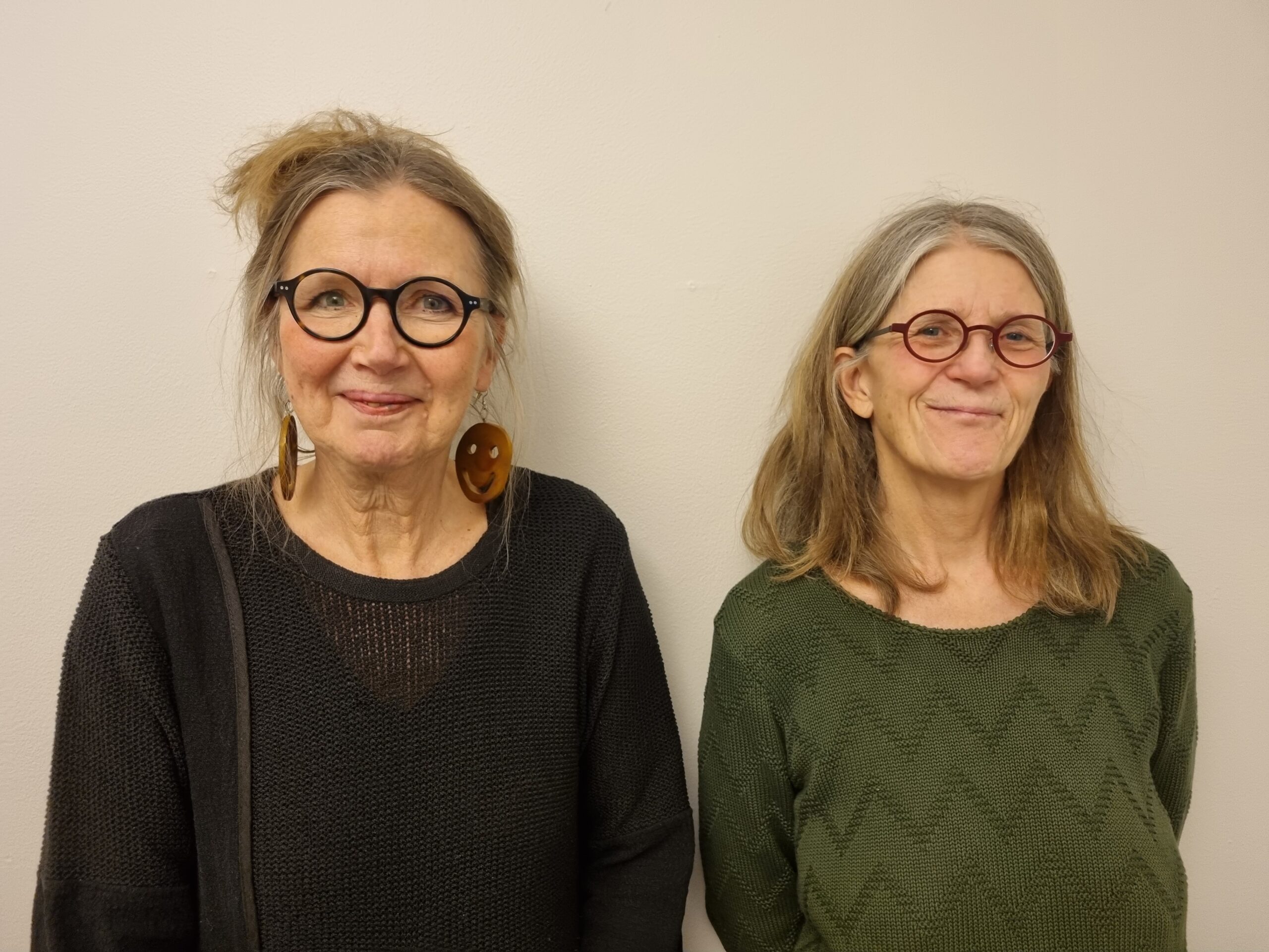 Inger och Ingela har båda glasögon och långt hår. Inger bär en svart tröja och Ingela en grön tröja med rundad hals.