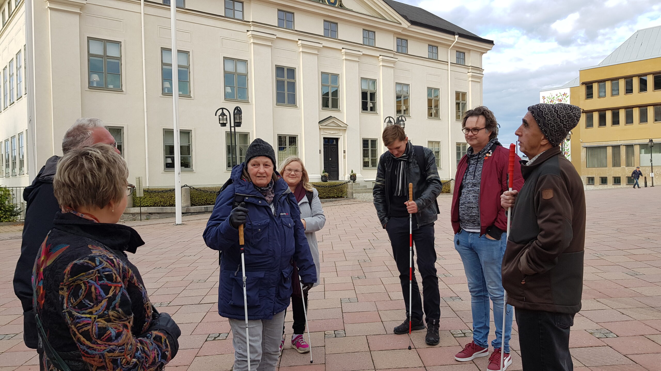 Sylvia håller i vita käppen omringad av politiker och synskadade på torget i Härnösand