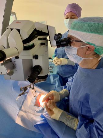 I blåa skyddskläder och blå hätta, vitt munskydd och handskar opererar kirurgen en ögonpatienten
